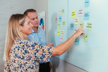 Foto av to personer som ser på en tavle med gule lapper.